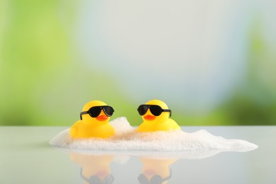 Photo of Cute rubber ducks and foam on table against blurred background