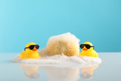 Photo of Cute rubber ducks, foam and sponge on table against light blue background