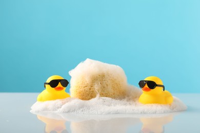 Photo of Cute rubber ducks, foam and sponge on table against light blue background