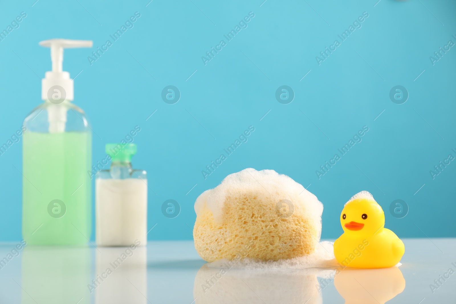 Cute rubber ducks, foam, sponge and bottles of cosmetic products on table against light blue background Photo of Cute rubber ducks, foam, sponge and bottles of cosmetic products on table against light blue background