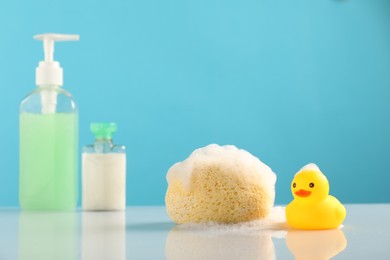 Photo of Cute rubber ducks, foam, sponge and bottles of cosmetic products on table against light blue background