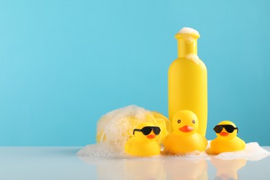 Photo of Cute rubber ducks, foam, sponge and bottle of shampoo on table against light blue background, space for text