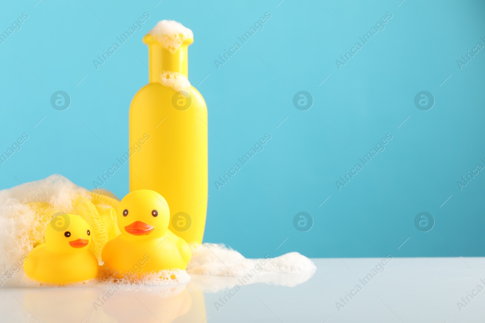 Cute rubber ducks, foam, sponge and bottle of shampoo on table against light blue background, space for text Photo of Cute rubber ducks, foam, sponge and bottle of shampoo on table against light blue background, space for text
