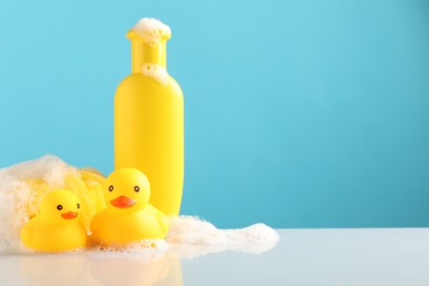 Photo of Cute rubber ducks, foam, sponge and bottle of shampoo on table against light blue background, space for text