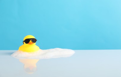 Photo of Cute rubber duck and foam on table against light blue background, space for text