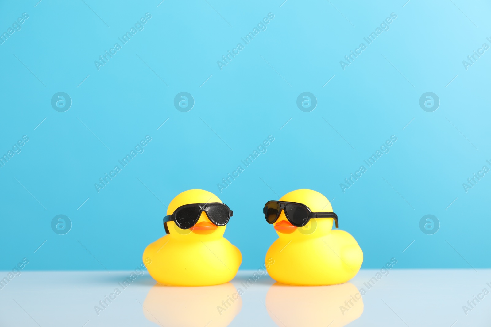 Two cute rubber ducks on table against light blue background Photo of Two cute rubber ducks on table against light blue background