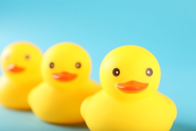 Photo of Three cute rubber ducks on light blue background, closeup