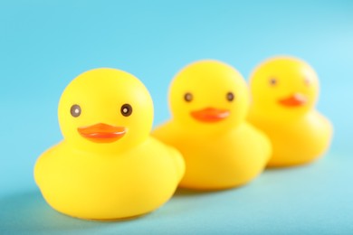 Photo of Three cute rubber ducks on light blue background, closeup