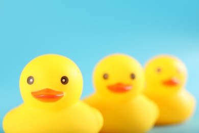 Photo of Three cute rubber ducks on light blue background, closeup