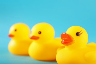 Photo of Three cute rubber ducks on light blue background, closeup