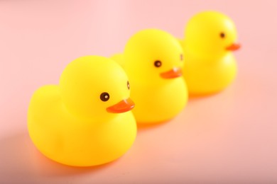 Photo of Three cute rubber ducks on pink background, closeup