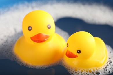 Photo of Cute rubber ducks floating in water with foam, closeup