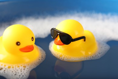 Photo of Cute rubber ducks floating in water with foam, closeup