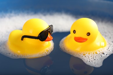 Photo of Cute rubber ducks floating in water with foam, closeup
