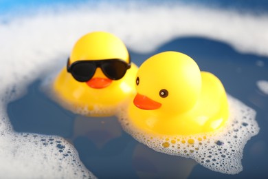 Photo of Cute rubber ducks floating in water with foam, closeup