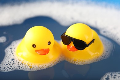 Photo of Cute rubber ducks floating in water with foam, closeup