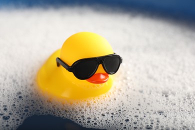 Photo of Cute rubber duck floating in water with bubbles, closeup