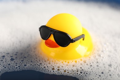 Photo of Cute rubber duck floating in water with foam, closeup