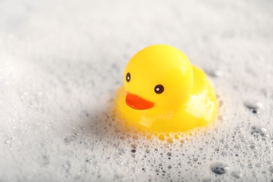 Photo of Cute rubber duck floating in water with foam, closeup