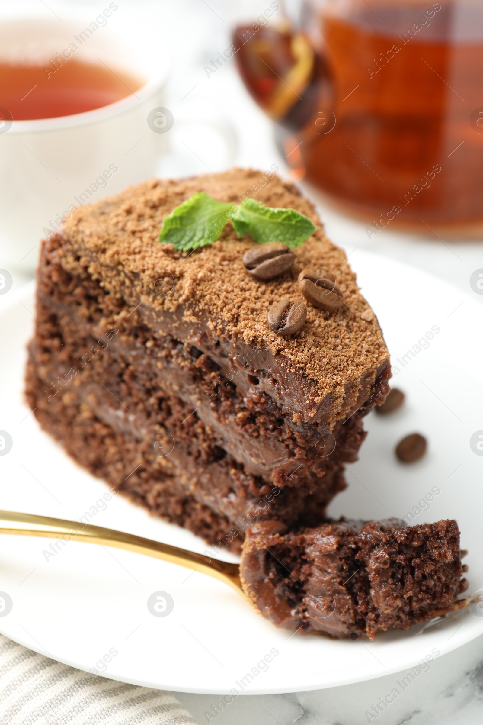 Photo of Piece of delicious chocolate cake with coffee beans, mint and fork on table, closeup