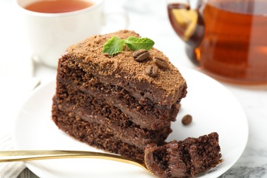 Photo of Piece of delicious chocolate cake with coffee beans, mint and fork on white marble table, closeup