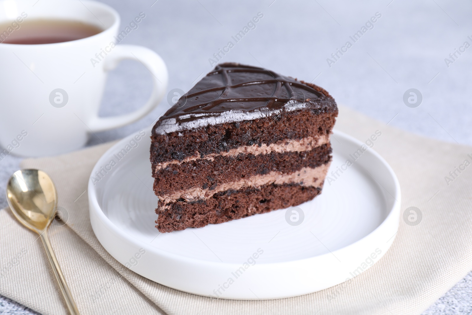 Photo of Piece of delicious chocolate cake and spoon on grey table, closeup