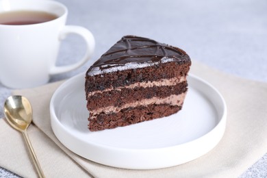 Photo of Piece of delicious chocolate cake and spoon on grey table, closeup