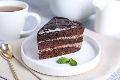 Photo of Piece of delicious chocolate cake with mint and spoon on grey table, closeup