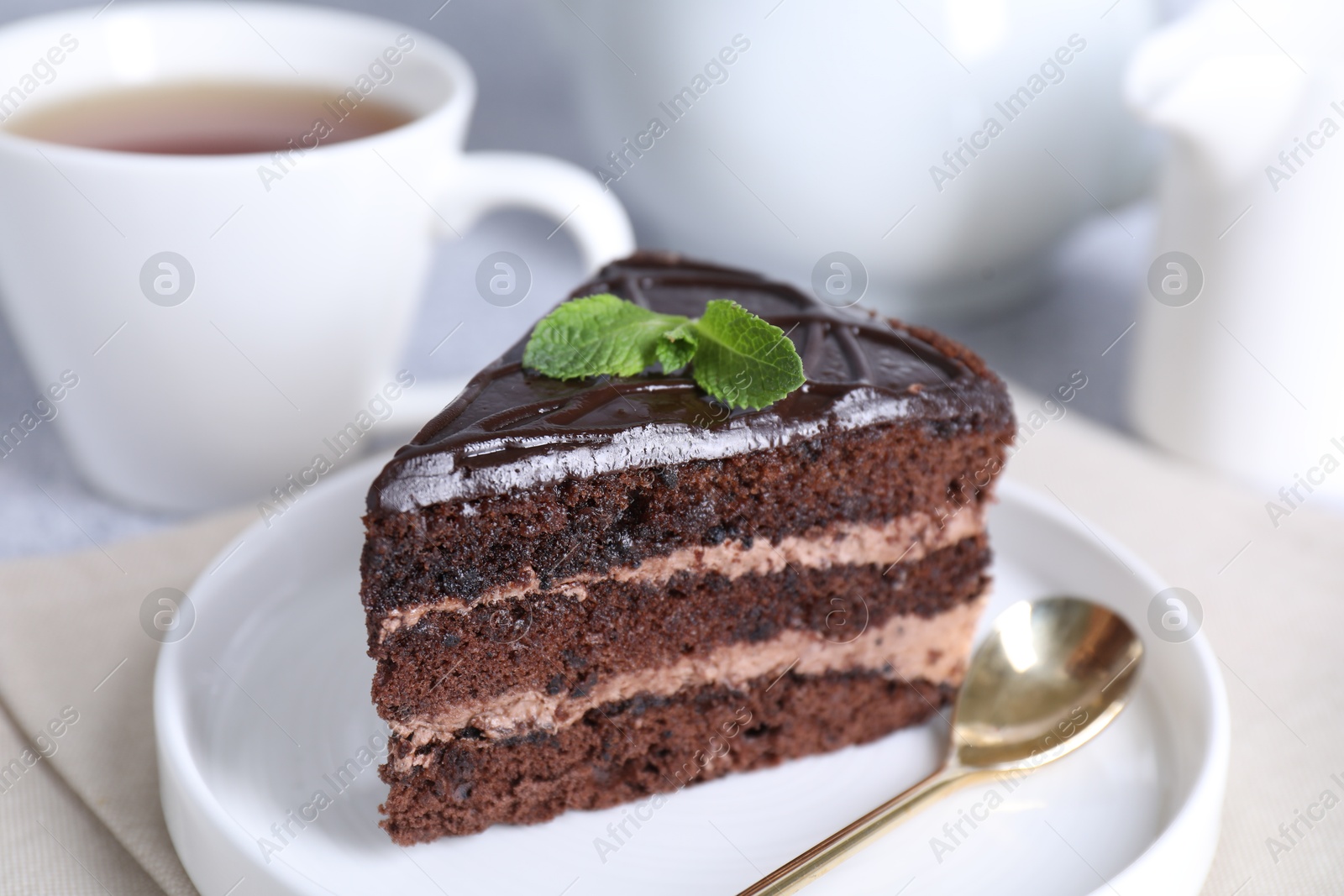 Piece of delicious chocolate cake with mint and spoon on light table, closeup Photo of Piece of delicious chocolate cake with mint and spoon on light table, closeup