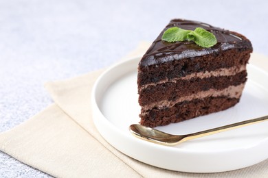 Photo of Piece of delicious chocolate cake with mint and spoon on grey table, closeup