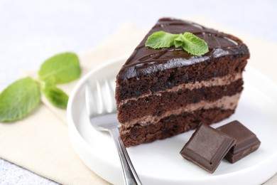 Photo of Piece of delicious cake, mint, chocolate and fork on light table, closeup