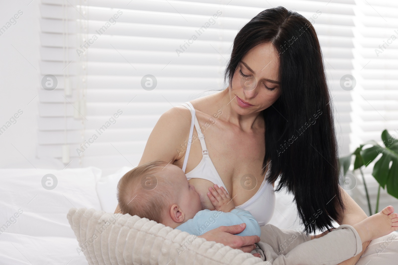 Photo of Mother breastfeeding her little baby on bed at home