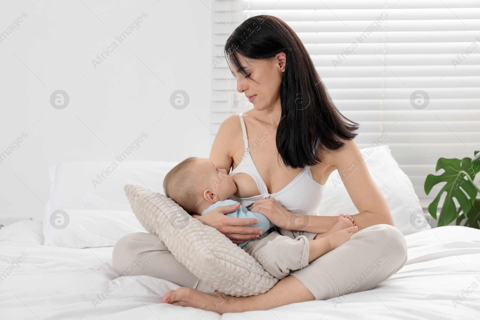 Photo of Mother breastfeeding her little baby on bed at home