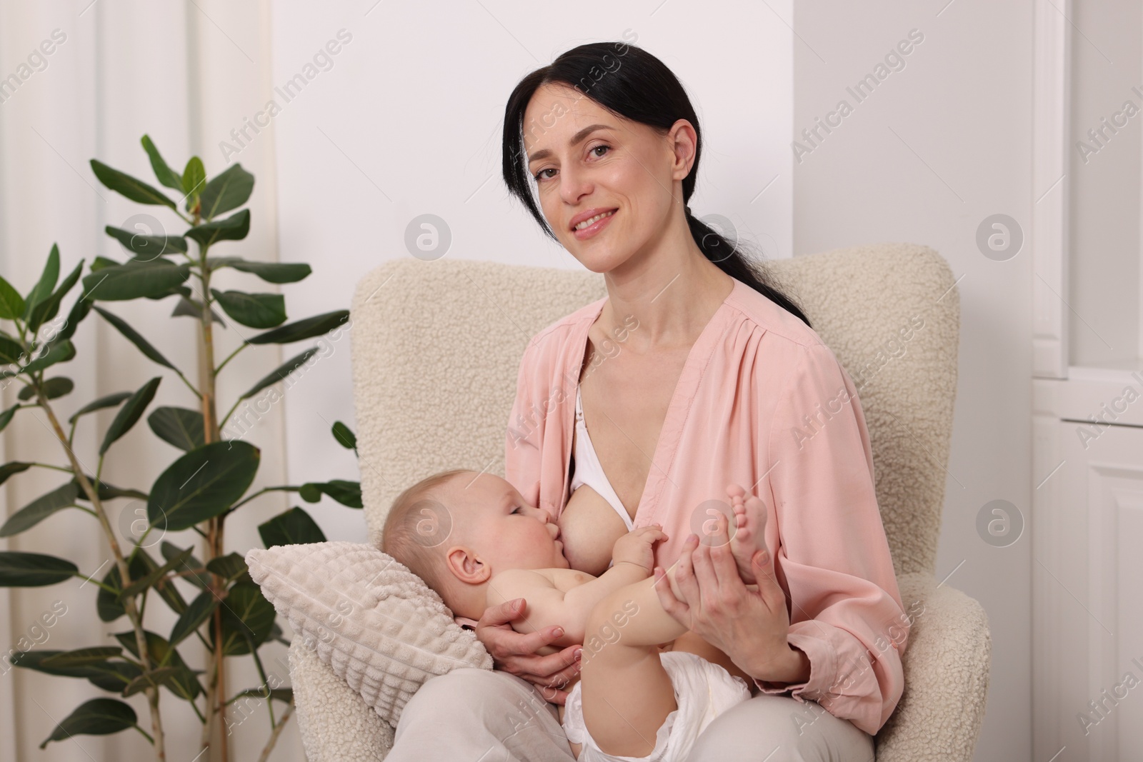 Smiling mother breastfeeding her little baby on armchair at home Photo of Smiling mother breastfeeding her little baby on armchair at home