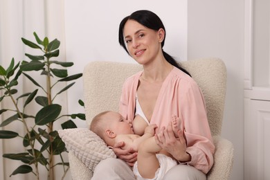 Photo of Smiling mother breastfeeding her little baby on armchair at home