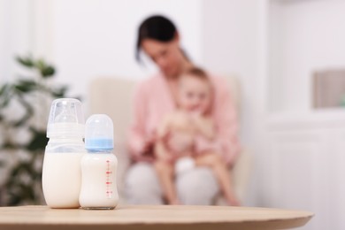 Photo of Mother with her little baby indoors, focus on bottles of milk