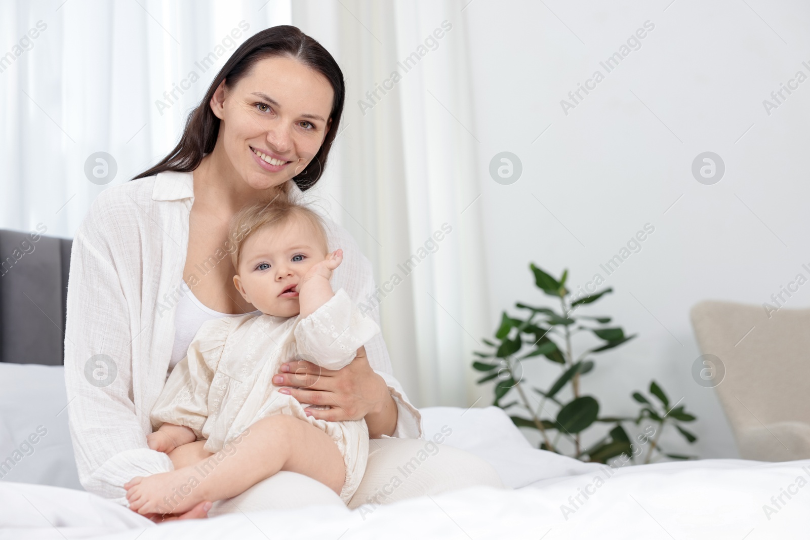 Smiling mother with her little baby on bed at home. Space for text Photo of Smiling mother with her little baby on bed at home. Space for text