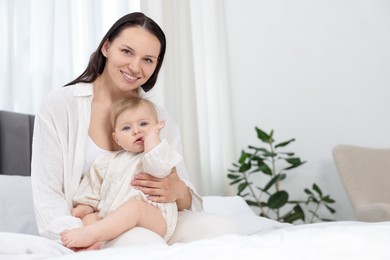 Photo of Smiling mother with her little baby on bed at home. Space for text