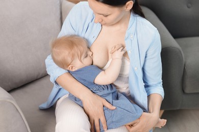 Photo of Mother breastfeeding her little baby on armchair indoors