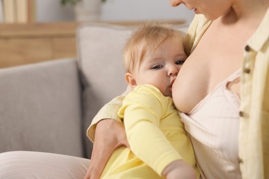 Photo of Mother breastfeeding her little baby on armchair indoors, closeup