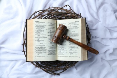 Photo of Judge's gavel, crown of thorns and Bible on white fabric, top view