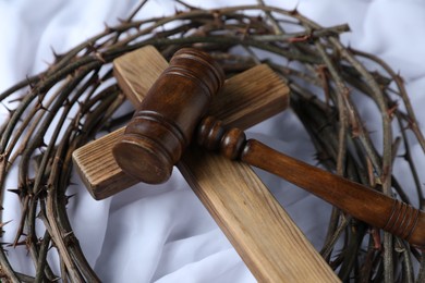 Photo of Judge's gavel, crown of thorns and wooden cross on white fabric, closeup