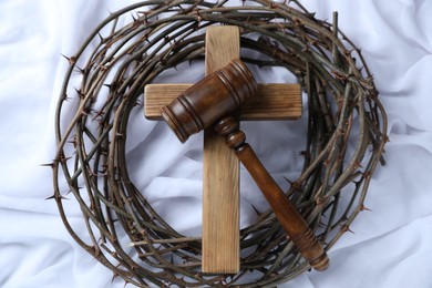 Photo of Judge's gavel, crown of thorns and wooden cross on white fabric, top view