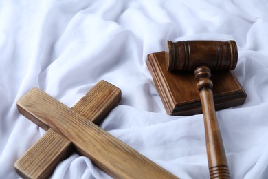 Photo of Judge's gavel and wooden cross on white fabric, above view