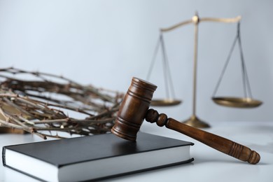 Photo of Judge's gavel, Bible, crown of thorns and scales on white table, closeup