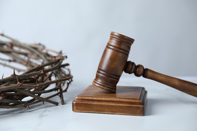 Photo of Judge's gavel and crown of thorns on white marble table, closeup