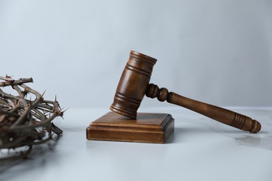 Photo of Judge's gavel and crown of thorns on white marble table