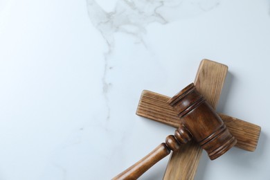 Photo of Judge's gavel and wooden cross on white marble table, top view. Space for text