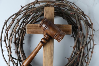 Photo of Judge's gavel, wooden cross and crown of thorns on white marble table, top view