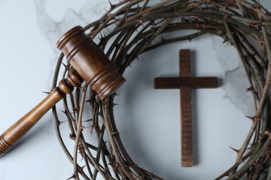 Photo of Judge's gavel, wooden cross and crown of thorns on white marble table, flat lay